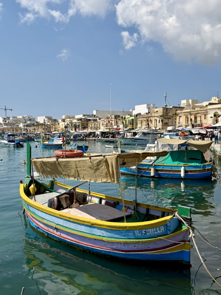 Jackson Rodriguez — A colorful traditional Maltese luzzu fishing boat named Il-Firilla sits moored in a bustling harbour. Marsaxlokk - Malta