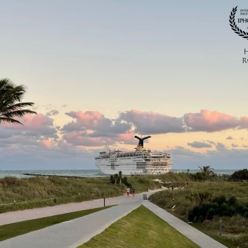 A cruise ship passes the tip of South Pointe Park in Miami Beach as it heads out of the Port of Miami at sunset, as the setting sun casts pink shadows on the clouds offshore.