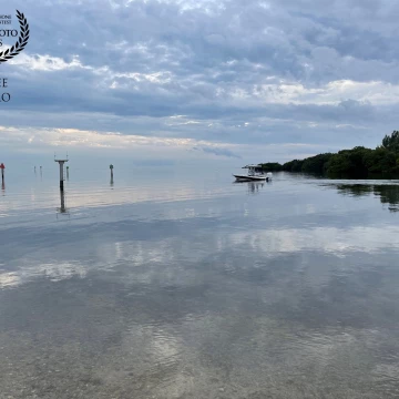 Clouds are reflected in the sea as a small boat motor out of the marina, past waymarkers set in the shallow water, at Matheson Park in Coral Gables, Florida.