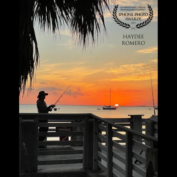 A fisherman casts a line at the Bill Baggs Cape Florida State Park on Key Biscayne in Florida as the sun sets behind an anchored sailing boat.