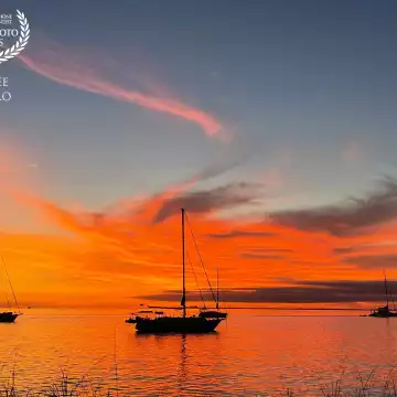 The setting sun paints swirling clouds orange and silhouette anchored sailing boats offshore from the Bill Baggs Cape Florida State Park on Key Biscayne in Florida.