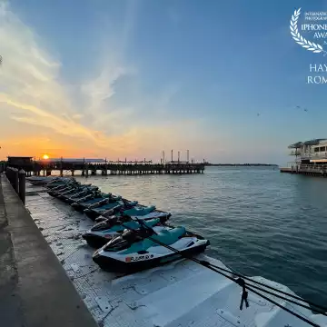 Jet skis for rent are lined up in the marina at Key West in Florida as the sun sets behind them over Sunset Pier full of people waiting for the sunset.