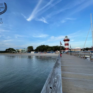 This is a view of the lighthouse at Harbour Town on Hilton Head Island in South Carolina, looking back from a pier at a small beach and light streaks of cloud.