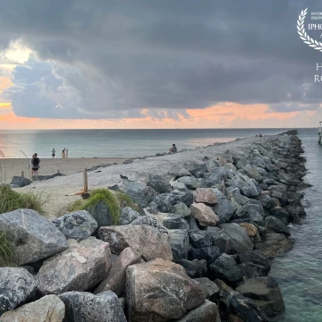 The opening sun ponds though tropical storm clouds off Miami Beach while tourists walk on the sand, take photos of daybreak or sit on the stones of a rock jetty at South Pointe Park in Miami Beach.