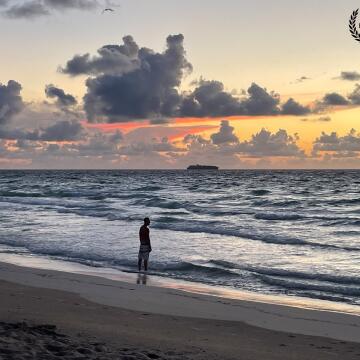 Early morning in Miami Beach you found many people waiting for the sunrise. A man watches as the sun rises off Miami Beach, Florida, sketching the clouds with red, orange and yellow colors.