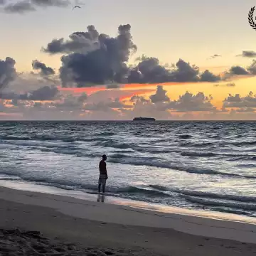 Early morning in Miami Beach you found many people waiting for the sunrise. A man watches as the sun rises off Miami Beach, Florida, sketching the clouds with red, orange and yellow colors.