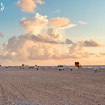 Towering clouds rise up over Miami Beach, Florida, casting red hues on the sand as the light of the morning starts to brighten the day.