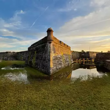 The creeping dusk sends colors across the sky and shadows over the swallow waters of the moat of the Castillo de San Marcos fort in St Augustine, Florida.