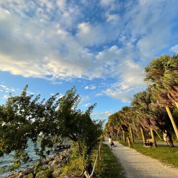 A family poses for photos on a pathway next to the water in Cape Florida state park on Key Biscayne, south Florida, while gusty winds bend the palms and send clouds rushing across the sky.