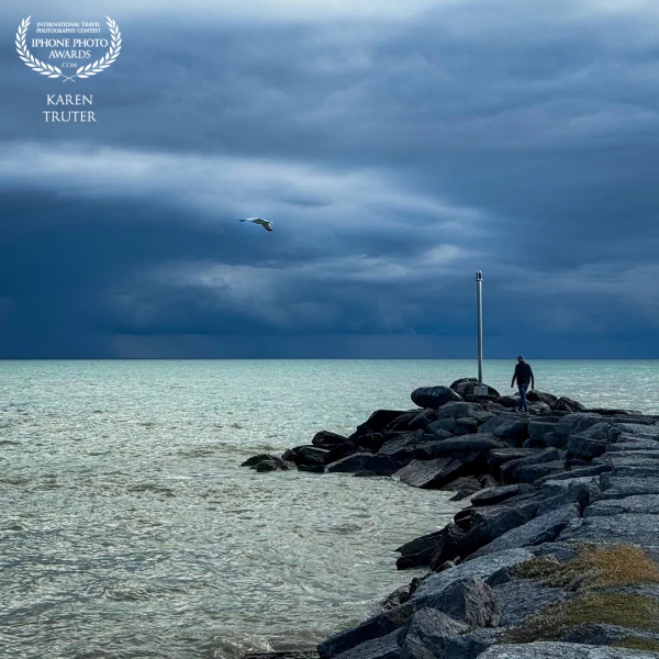 Wicklow Beach, Ontario. A stormy sky was the back drop that emphasized the azure blue colour of Lake Ontario as my friend walked out to the end of the breakwater making this a perfect photo op.