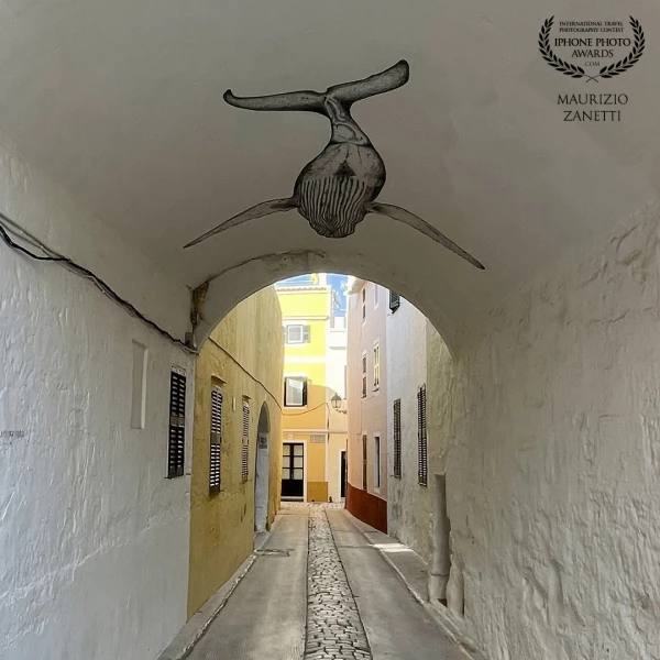 The painted whale appears to fly under the arch of an alley in Ciutadela, island of Menorca