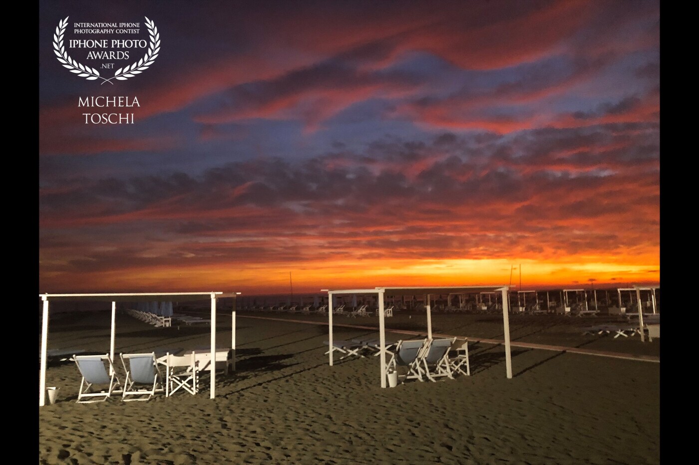 Tuscany. Forte dei Marmi. A play of lights and a breathtaking scenery. The evening light comes on illuminating the first tents and the beach. In the background an extraordinary sunset.