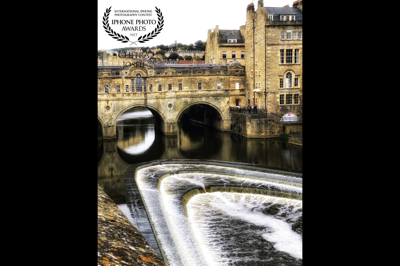 Here we have a famous architectural sensation, “Pulteney Bridge” in the wonderful city of Bath, United Kingdom. Fantastic Georgian architecture with shops across its full span on both sides. Do you see the eye-catching view of River Avon, flowing below the bridge? And the stunning radiance, that the gushing water emits? That's the beauty of the place.