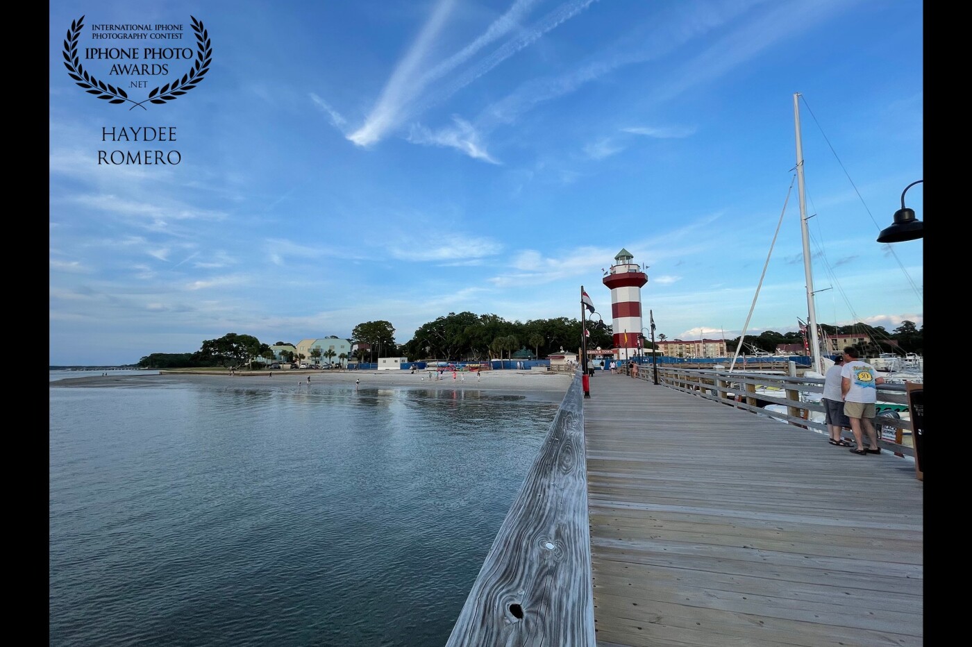 This is a view of the lighthouse at Harbour Town on Hilton Head Island in South Carolina, looking back from a pier at a small beach and light streaks of cloud.