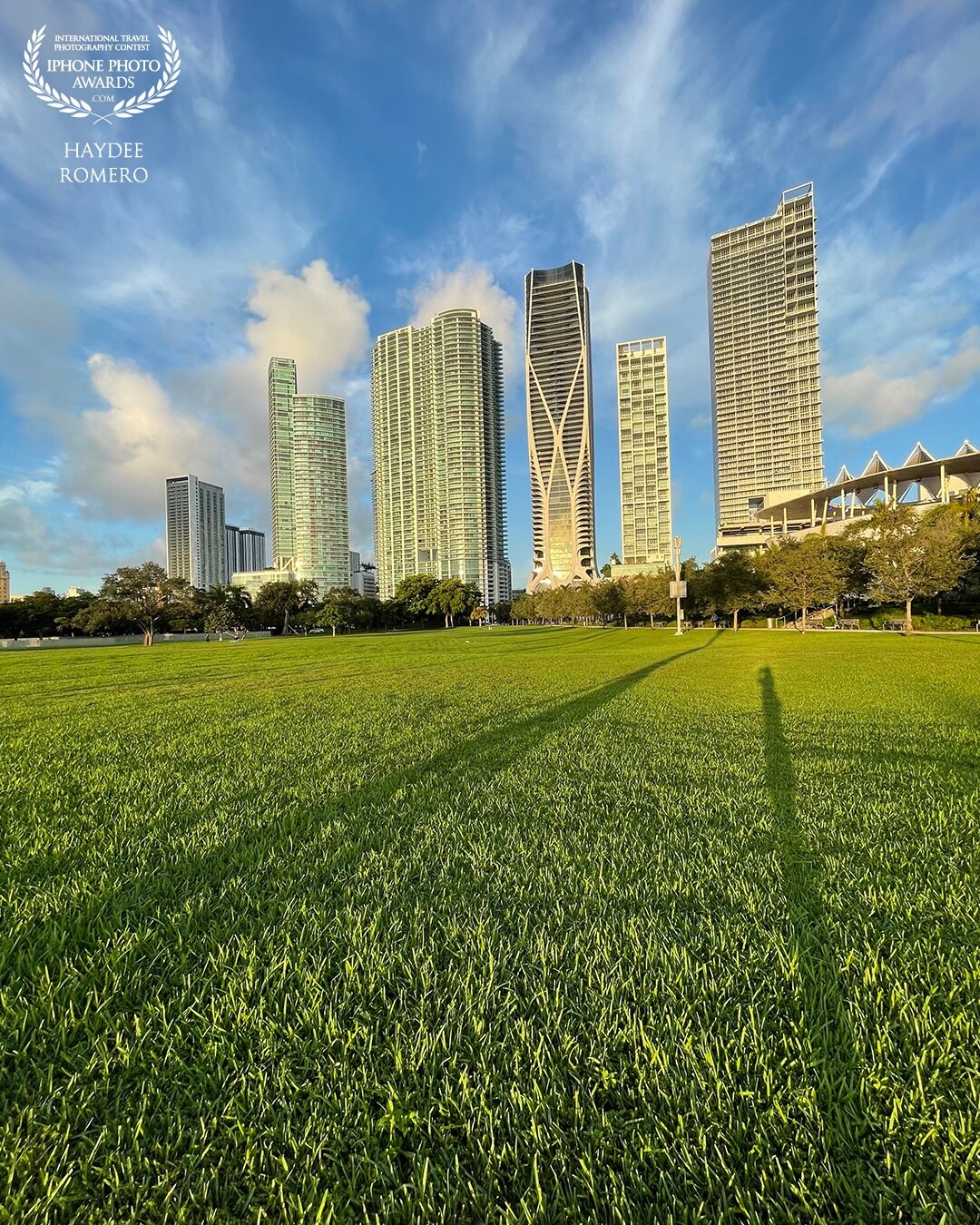 Modern skyscrapers stretch up towards clouds that appear to be racing across the sky behind the Perez Art Museum and the adjacent park in downtown Miami.