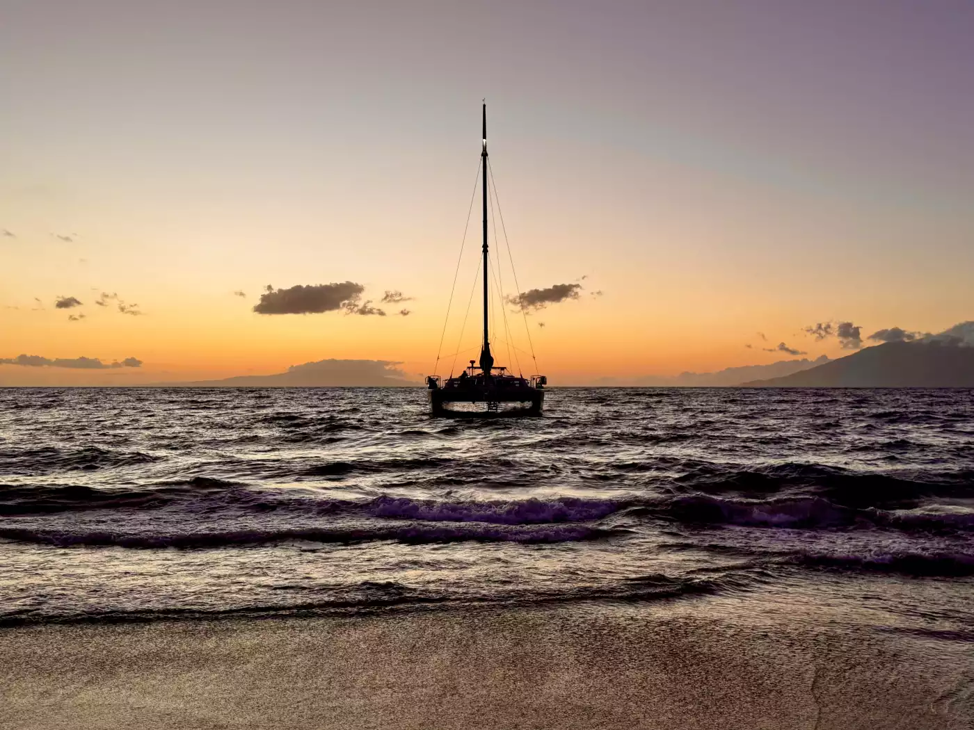 A catamaran silhouetted against a canvas of sunset hues, drifting through one of nature’s most beaut...